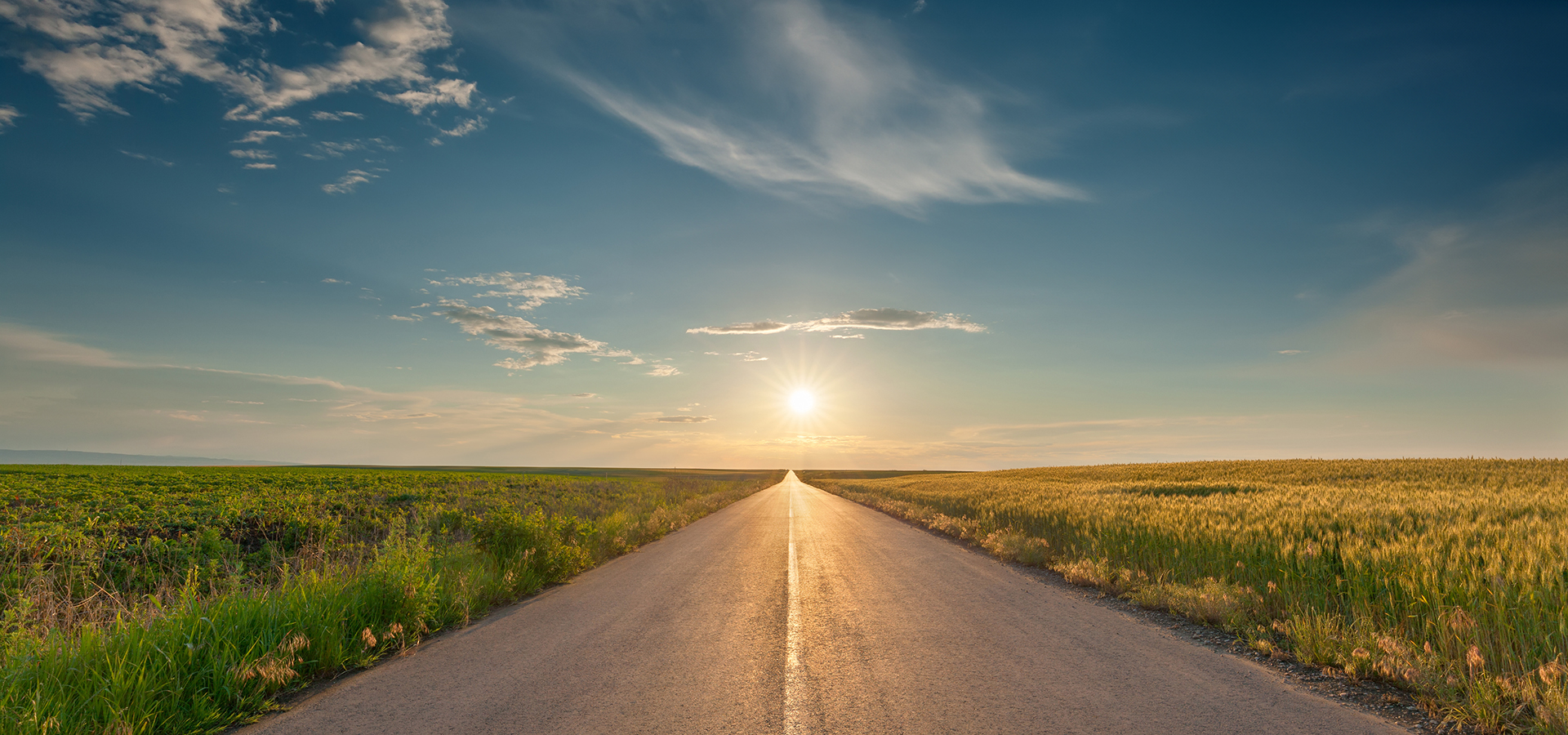 Conduire sur une route asphaltée vide à travers les champs de blé et de soja vers le soleil couchant.