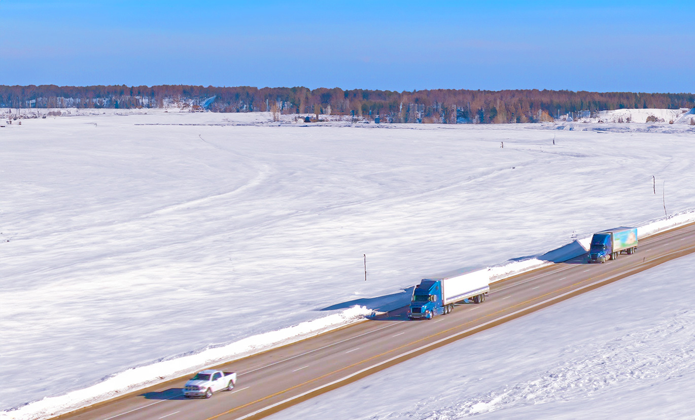 Semi Trucks traveling on freeway in a snowy landscape