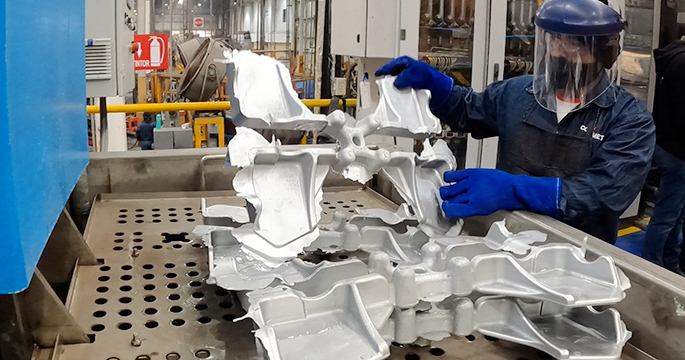 Empleado sacando piezas de aluminio fundido del equipo de fabricación