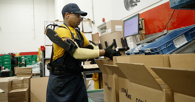 Trabajador levantando un extremo de rueda desde una caja mientras usa un exotraje para protegerse